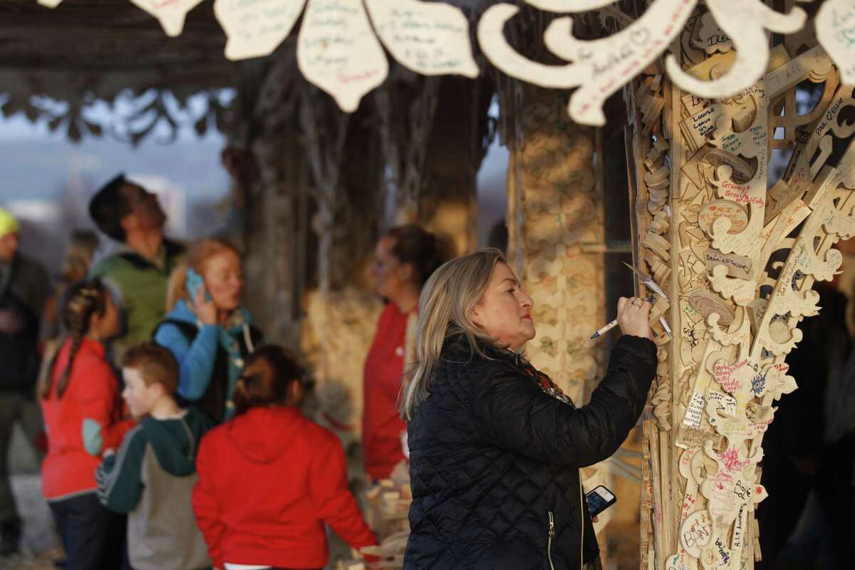 In this Photo taken Wednesday March 18, 2015, a woman writes a message on the intricately hand crafted wooden tower, on a hill overlooking Londonderry, Northern Ireland. Attracting thousands of people to write messages, the 72 foot tall (22 meter) wooden tower designed by American sculptor David Best, is scheduled to be burned to the ground Saturday night. In a region normally marked by divisions, and where bonfires are normally burned as acts of sectarian division, this ornate wooden tower is attracting both Protestant and Catholic admiration, in an atmosphere of harmony. (AP Photo/Peter Morrison)