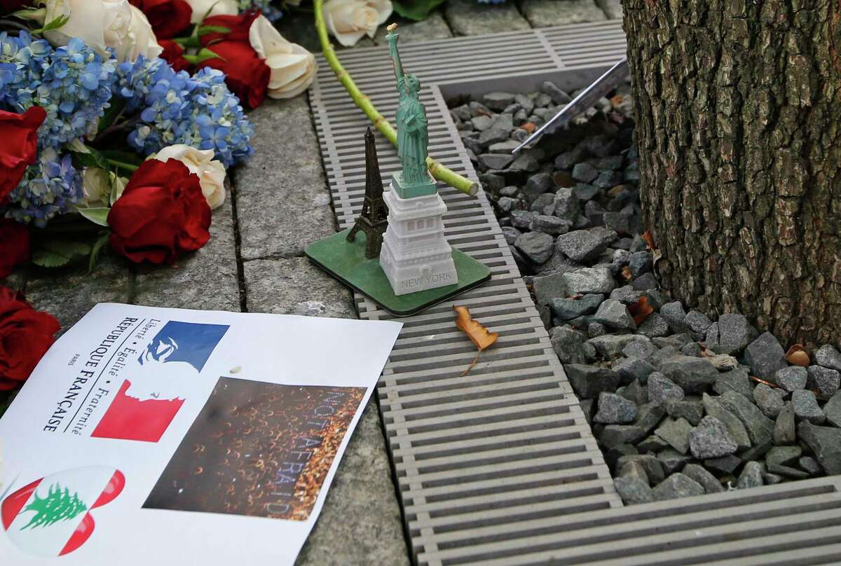 Items left at the foot of the Survivor Tree, part of the 9/11 Memorial, following a tribute to victims of the Paris terrorist attacks, include a replica of the Eiffel Tower and another of the Statue of Liberty, along with red, white and blue flowers in New York.