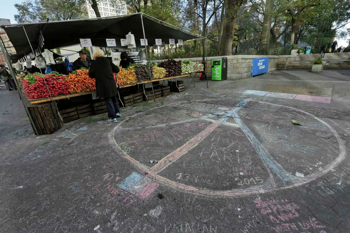 A woman shops for produce next to a peace sign drawn in solidarity to the people of Paris at the framers market in New York’s Union Square, Saturday, Nov. 14, 2015. French officials say several dozen people were killed in shootings and explosions at a theater, restaurant and elsewhere in Paris on Friday.