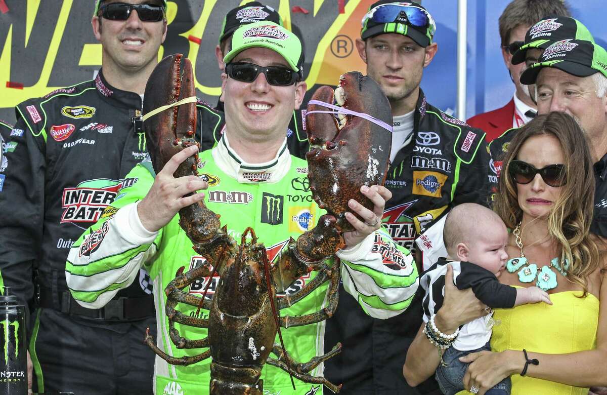 Kyle Busch holds the Loudon lobster trophy in Victory Lane, as his wife, right, Samantha holding son Brexton looks on.