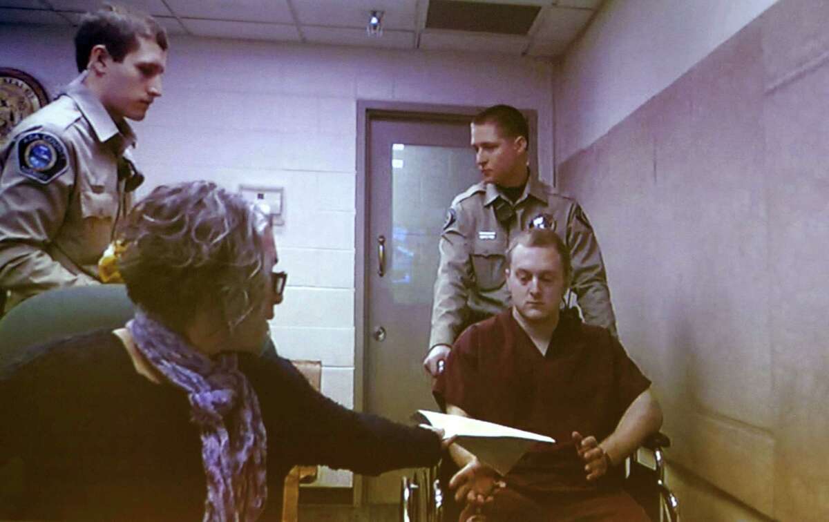 Adam Dees (right, in wheelchair) is pictured on a video screen during an arraignment at the Ada County Courthouse in Boise, Idaho Thursday March 12, 2015. Bond was set at $2 million for Dees, based upon his possible involvement in the murders of Theodore, Delores and Thomas Welp. Dees is currently charged with three counts of grand theft, three counts of forgery and a single count of possessing a concealed weapon. (AP Photo/The Idaho Statesman, Kyle Green)