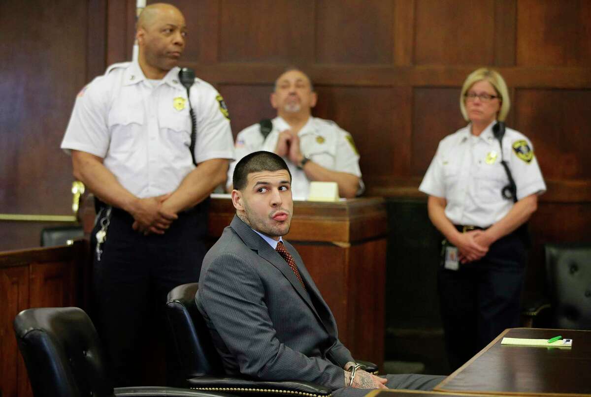 Former New England Patriots NFL football player Aaron Hernandez sits at the defendant’s table while his attorneys participate in a sidebar discussion during his arraignment at Suffolk Superior Court on May 21, 2015 in Boston, on a charge of trying to silence a witness in a double murder case against him by shooting the man in the face.