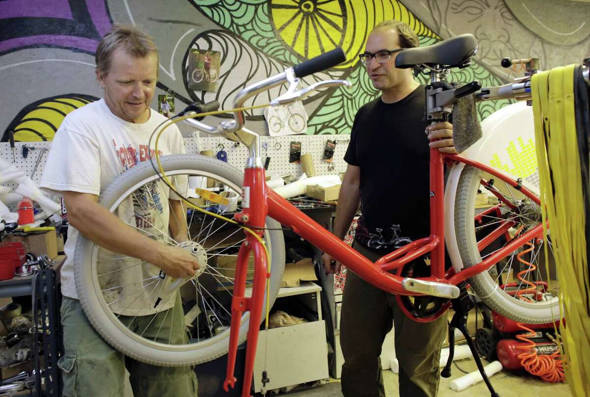 Avery Pack, president of Republic Bike, right, talks with employee Tim Hignett, left, as he assembles a fleet bicycle manufactured at Republic Bike, in Dania Beach, Fla.