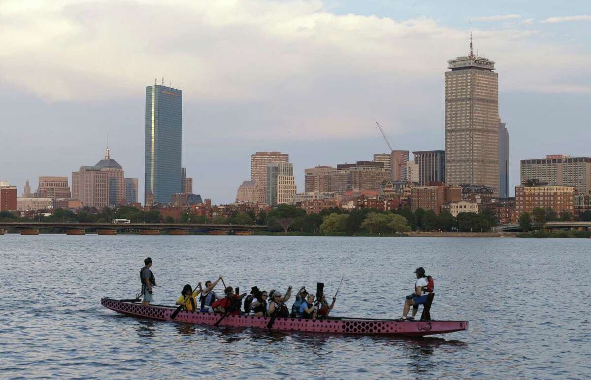 A boat glides along the Cambridge, Mass., side of the Charles River in front of the Boston skyline.