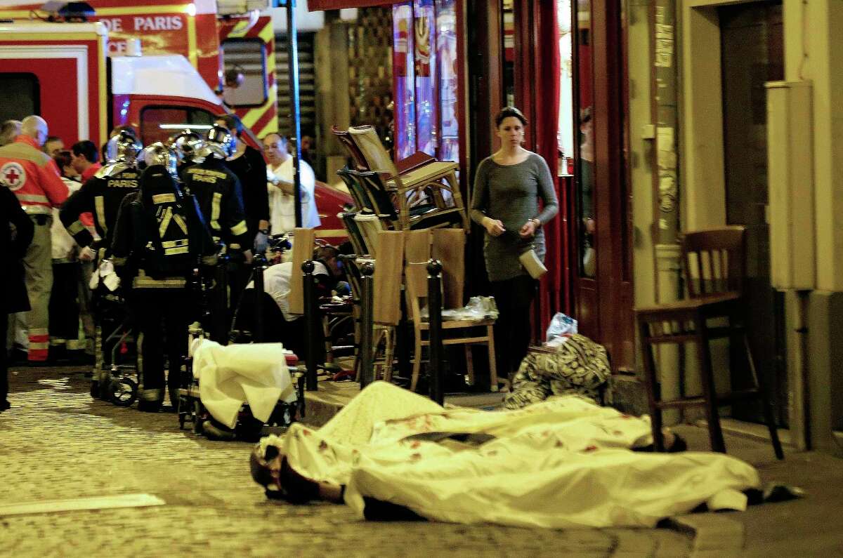 In this Nov.13, 2015, file photo, a woman watches victims lying outside Le Belle Equipe restaurant in Paris. All the attackers and accomplices so far identified were raised in Europe, native French speakers with roots in the marginalized immigrant communities of France and Belgium. Minor players — like the man who rented a room to the attacks’ mastermind, Abdelhamid Abaaoud — have a degree or two of separation in an underworld of drugs, fraud and theft.