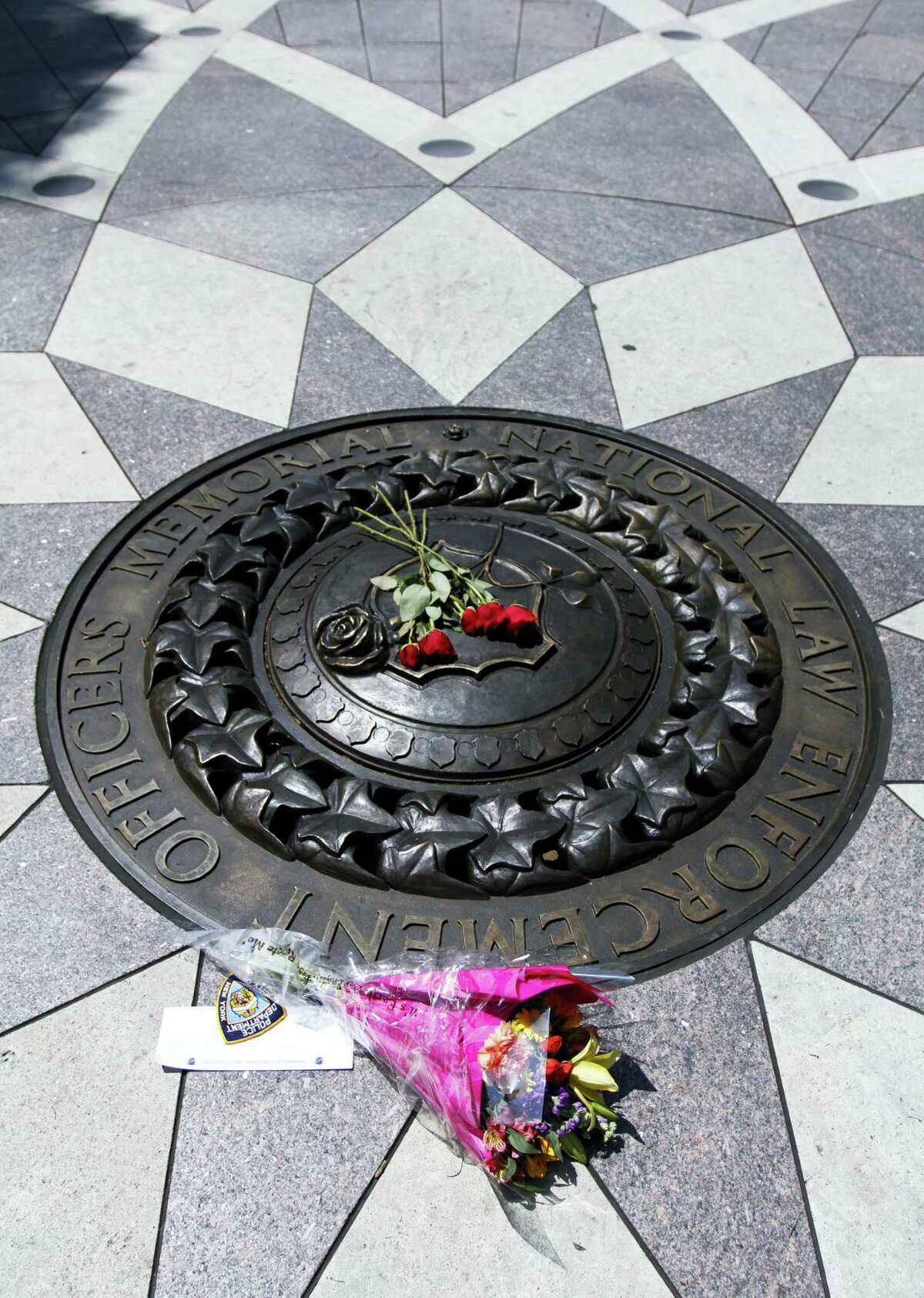Five red roses and a bouquet of flowers with a note of support for the Dallas Police Department lies on the bronze medallion at the National Law Enforcement Officers Memorial in Washington, Friday, July 8, 2016. Five officers were killed in Dallas on Thursday.