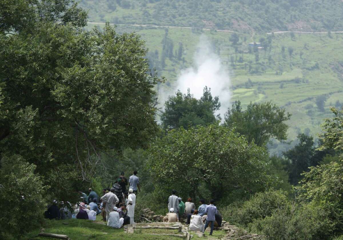 Smoke rises behind from a mortar shell fired by Pakistani troops as Indian villagers sit during the funeral of Indian civilian Sarpanch Karamat Hussain who was killed in Pakistani shelling at Balakot sector in Poonch, Jammu and Kashmir, India on Aug.16, 2015. Indian and Pakistani troops traded heavy gunfire and mortar rounds for a seventh day Sunday along the highly militarized line of control dividing the disputed Himalayan region of Kashmir between the two archrivals, officials said.