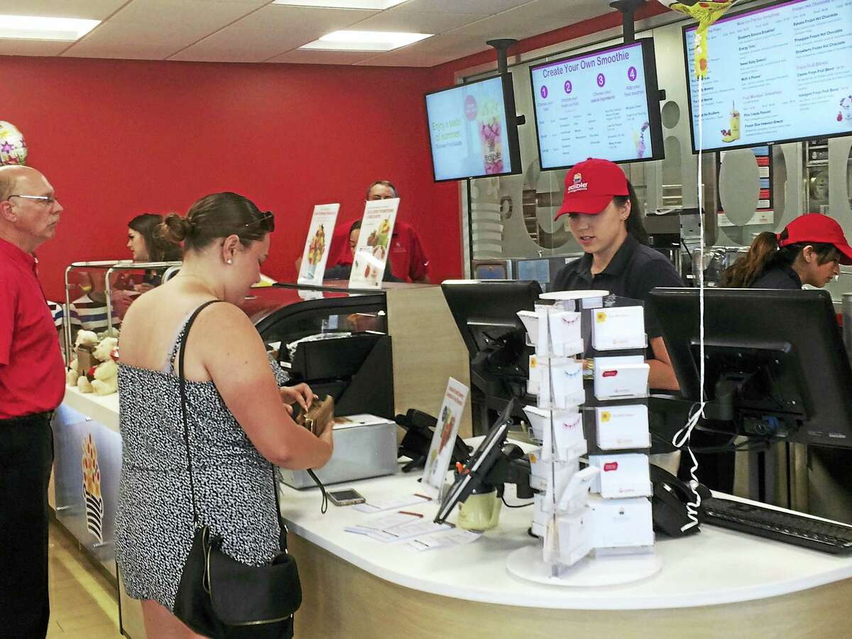 A customer pays for her fresh fruit smoothie Wednesday at the new Edible To Go store in Wallingford, in the Edible Arrangements headquarters.