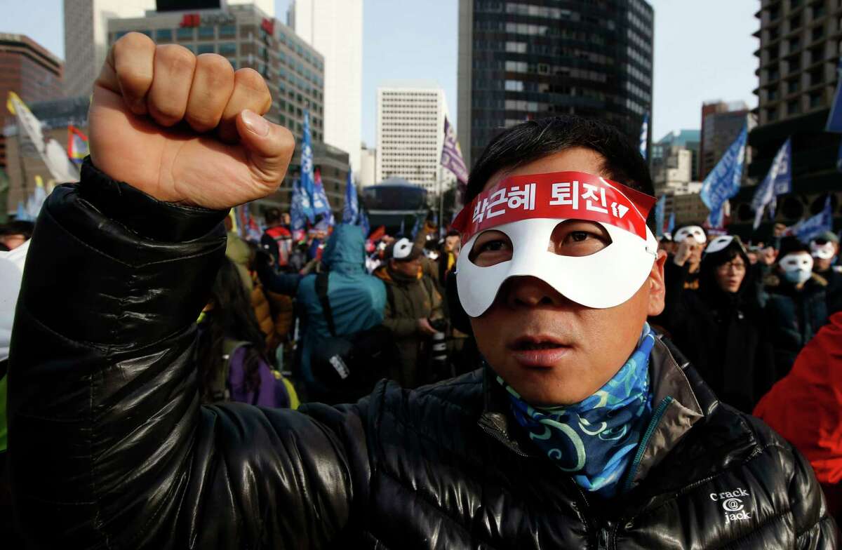 South Korean protesters attend an anti-government rally in downtown Seoul, South Korea, Saturday, Dec. 5, 2015. Wearing white half-masks and carrying flowers and banners, thousands of South Koreans marched in Seoul on Saturday against conservative President Park Geun-hye, who had compared masked protesters to terrorists after clashes with police broke out at a rally last month.