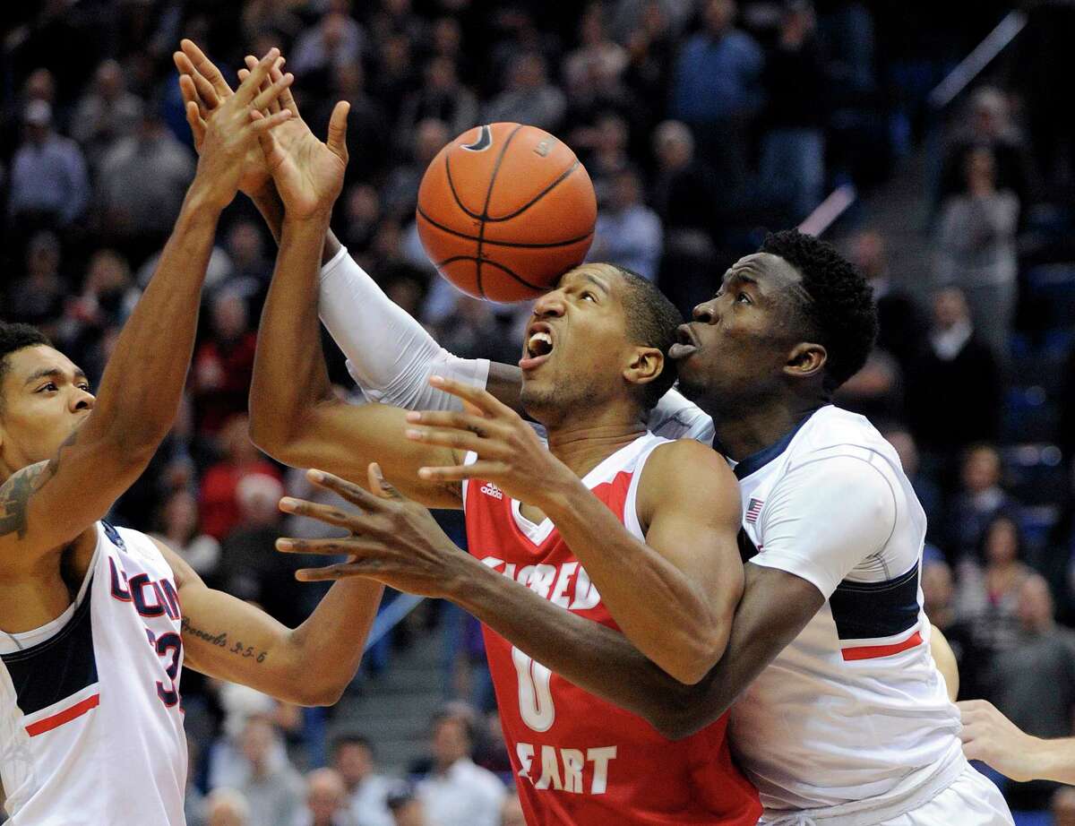 Sacred Heart’s Jordan Allen (0) vies for the ball with Connecticut’s Shonn Miller, left, and Amida Brimah