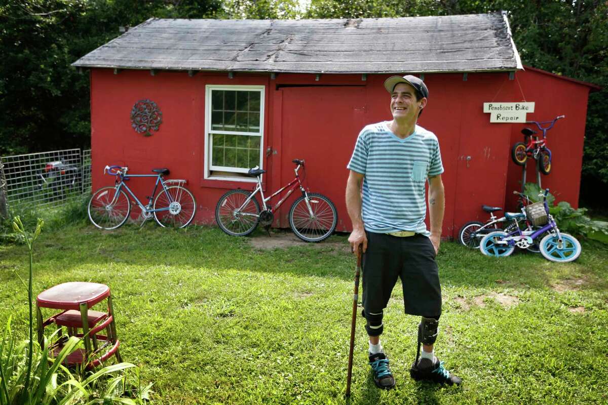 In Thursday, July 30, 2015, photo Ryan Kinsella poses outside his bicycle repair business in Penobscot, Maine. Kinsella broke his back in a rock climbing accident in 2002. The accident left him with partially paralyzed legs. He is recovering from a long battle with hepatitis C, which he contracted by sharing IV drug needles.