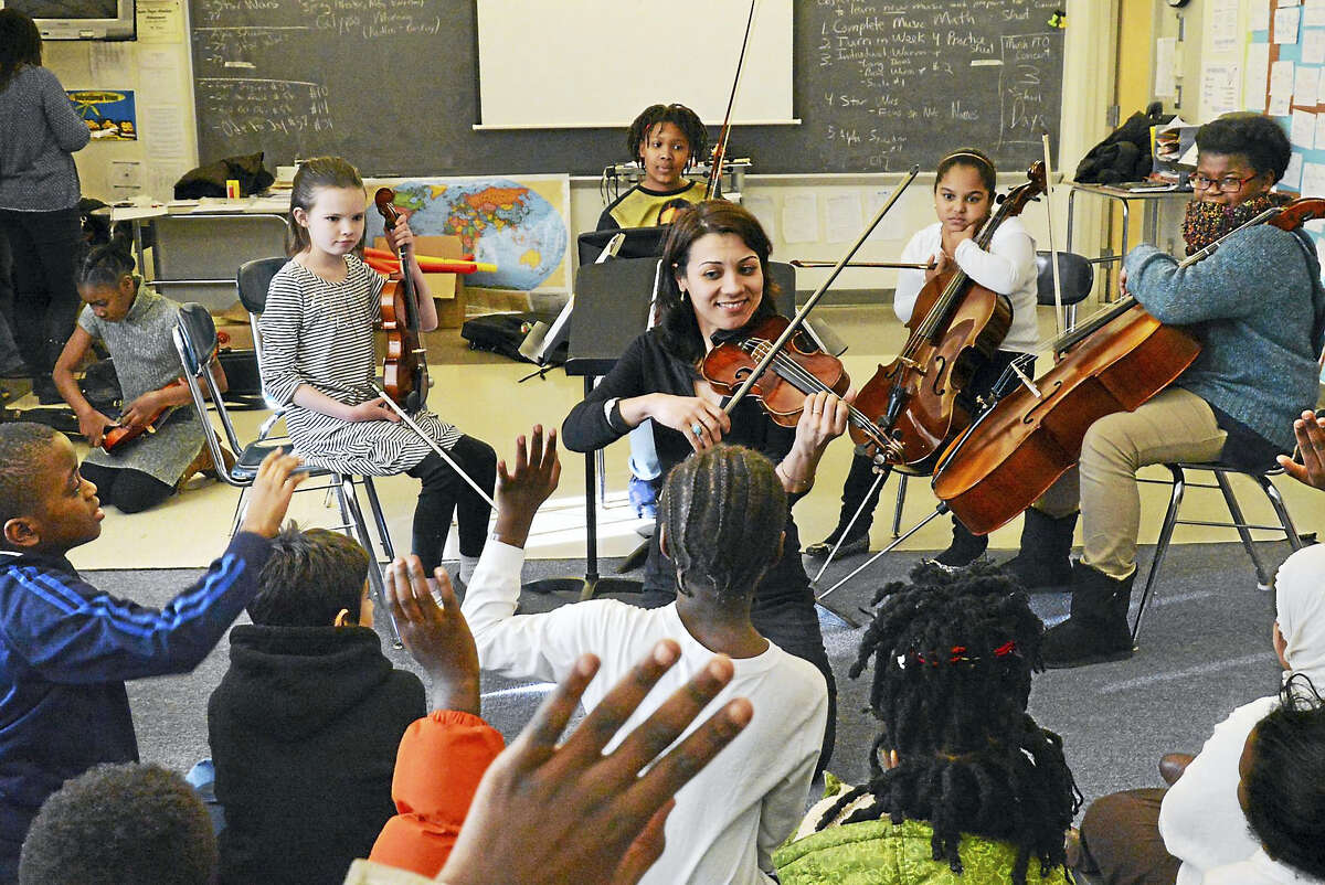 Violinist/teacher Yaira Matyakubova, backed by Music Haven students, plays for a group of refugee/immigrant children (foreground) in a visit to the after-school program at Fair Haven School.