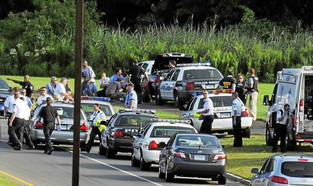 Employees of Hartford Distributors sit behind a police car after evacuating the building in Manchester, Conn. on Aug. 3, 2010. Ormar Thornton, a driver for Hartford Distributors, killed eight people, plus himself at the beer distribution company that Tuesday morning.