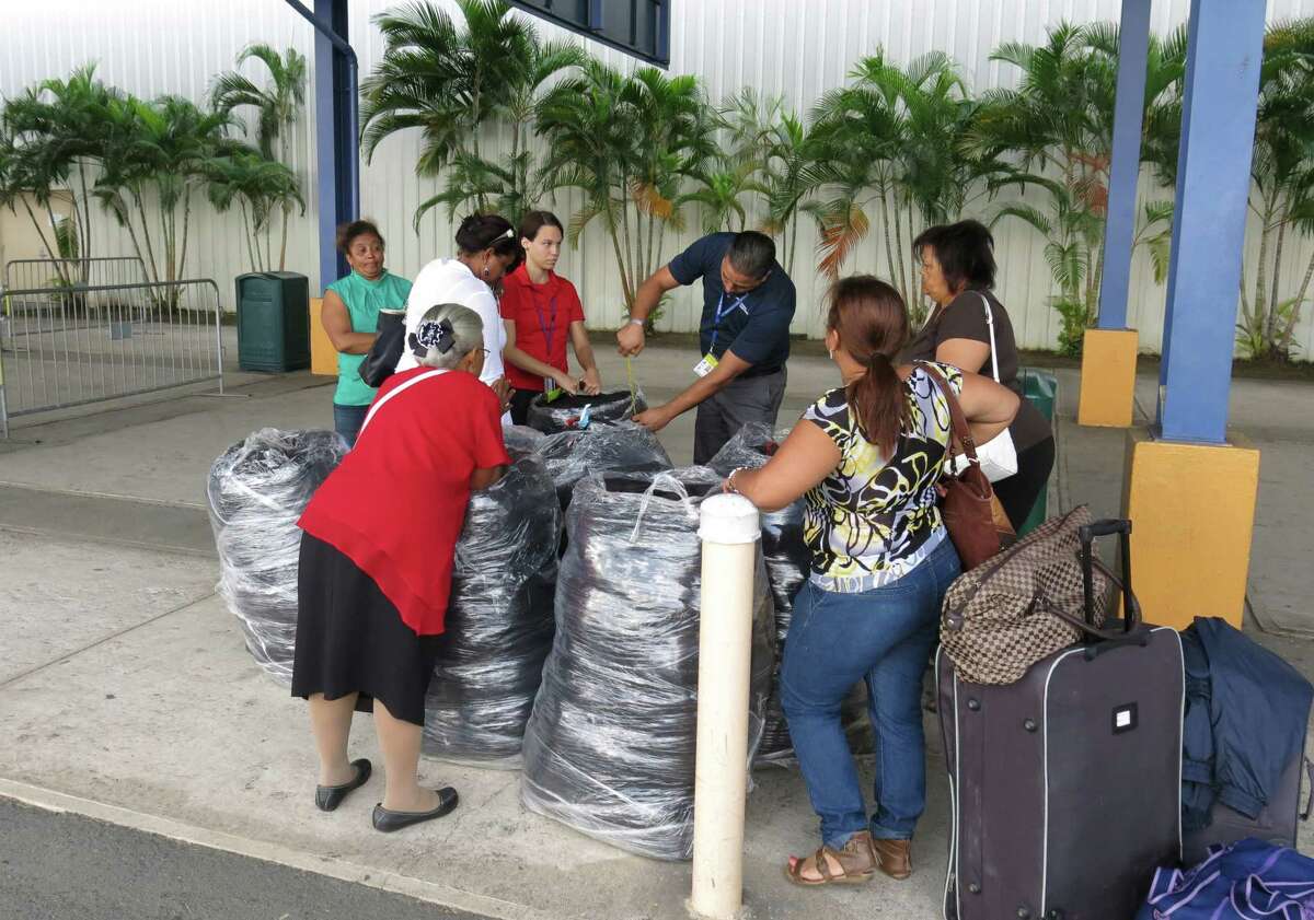 In this Jan. 22, 2016 photo, workers measure luggage size as passengers in San Juan, Puerto Rico wait to board a ferry headed for the Dominican Republic. A growing number of financially strapped Puerto Ricans are moving to the neighboring Caribbean country to open businesses and escape economic chaos that has scared away even many Dominican migrants.
