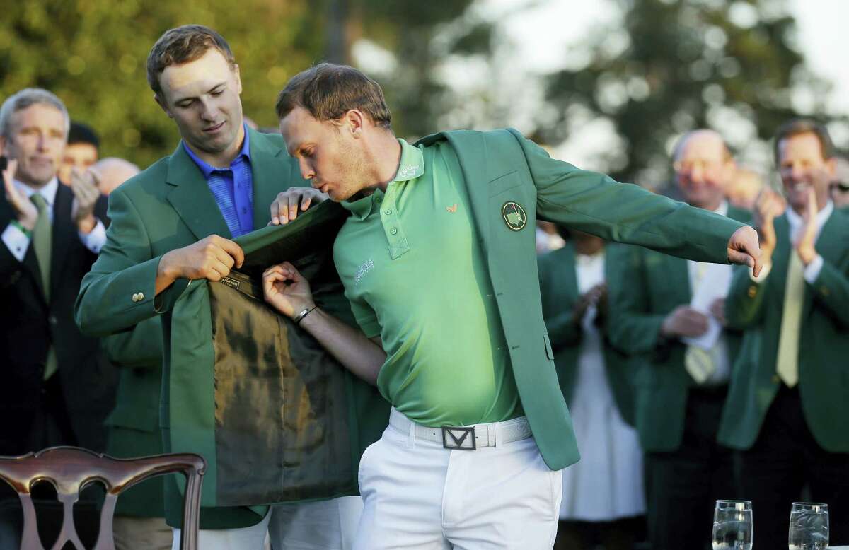 Defending champion Jordan Spieth, left, helps 2016 Masters champion Danny Willettput on his green jacket following the final round of the Masters Sunday.
