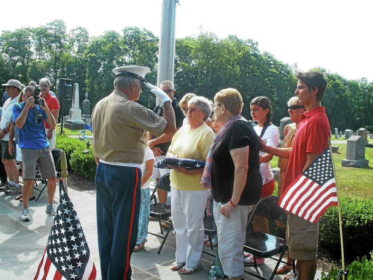 Barbara Bongiolatti hands over the flag that will be flown in honor of her late husband, Private 1st Class U.S. Army veteran Emilio Bongiolatti, at the All Wars Memorial in Bantam until Sept. 5. ?