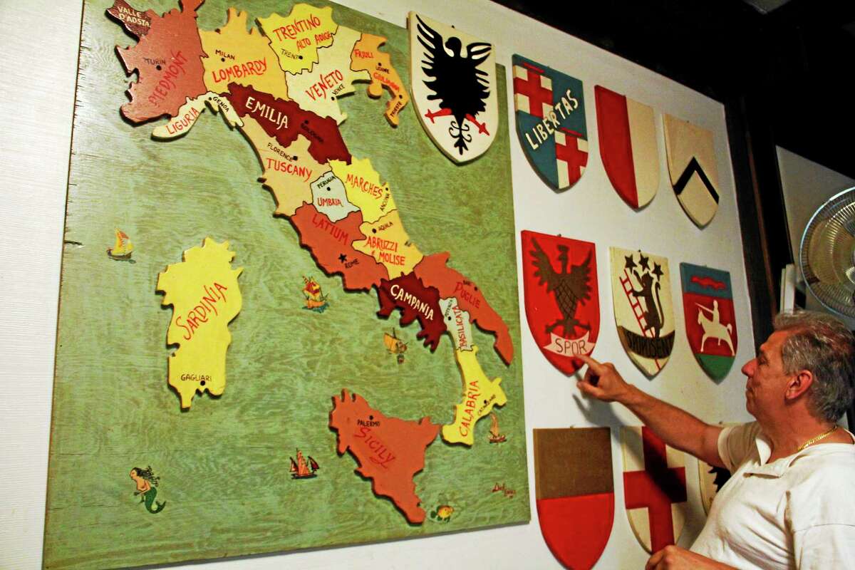 Club president Bruce Harrison points at an art display with a map of Italy and coat of arms inside the Order of the Sons of Italy on Center Street on June 24 in Torrington.