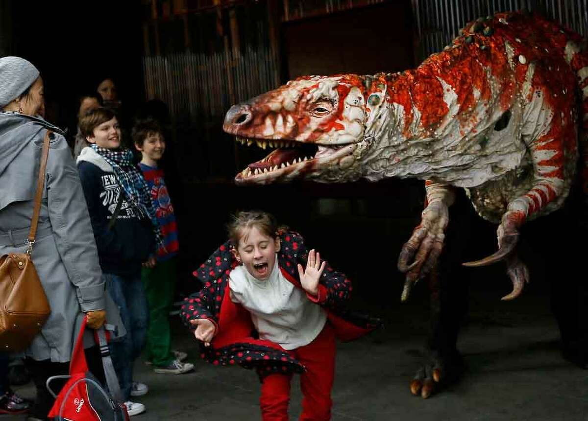 Children react as a carnivorous theropod known as the Australovenator dinosaur walks through crowds along the Southbank, in London, Monday, Feb. 18, 2013. The dinosaur is one of many that can be visited at the Erth's Dinosaur Petting Zoo, visiting from Australia, the creatures can be touched and fed at the Southbank Centre. (AP Photo/Kirsty Wigglesworth)