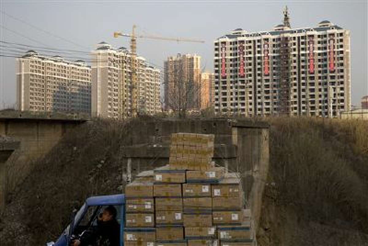 A man talks on a mobile phone inside his tricycle cart loaded with goods near under-construction residential buildings in Changsha, in China's Hunan province. U.S. investors are being hit with new worries from overseas just as the economy at home appears to be strengthening. (AP Photo/Andy Wong, File)