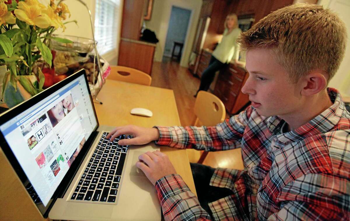 In this Oct. 24, 2013 photo, Mark Risinger, 16, checks his Facebook page on his computer as his mother, Amy Risinger, looks on at their home in Glenview, Ill. The recommendations are bound to prompt eye-rolling and LOLs from many teens but an influential pediatrician's group says unrestricted media use has been linked with violence, cyber-bullying, school woes, obesity, lack of sleep and a host of other problems. Mark’s mom said she agrees with restricting kids’ time on social media but that deciding on other media limits should be up to parents. (AP Photo/Nam Y. Huh)