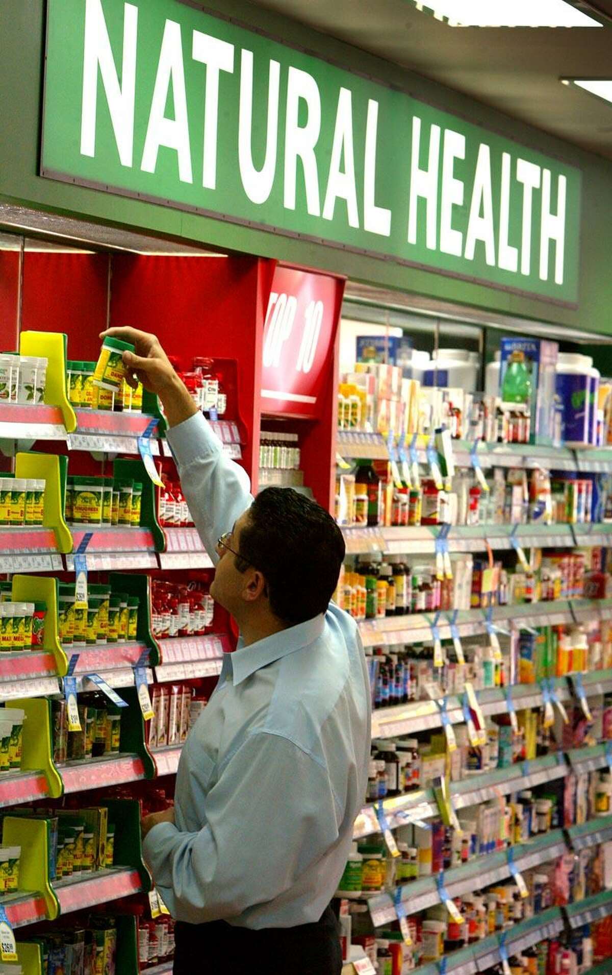 Store worker Sam Issa checks the brand names of rows of herbal, vitamin and mineral pill products at a suburban pharmacy in Sydney April 29, 2003. Australians were urged not to panic over the biggest medical recall in the nation's history which could spread to thousands of over-the-counter drugs and exports of non-prescription medicines in Asia and Europe. Pan Pharmaceuticals, Australia's largest maker of herbal, vitamin and mineral pills (better known as 'complimentary medicines'), is accused of potentially harmful safety and quality breaches in making its own products and goods for other brands. The government's Therapeutic Goods Administration (TGA) has warned Australians to delay taking vitamin and herbal supplements, and the Pharmecy Guild of Australia said confusion reigned as to which products they had to advise their members to remove from their shelves until they new which ones contained Pan ingredients. REUTERS/David Gray