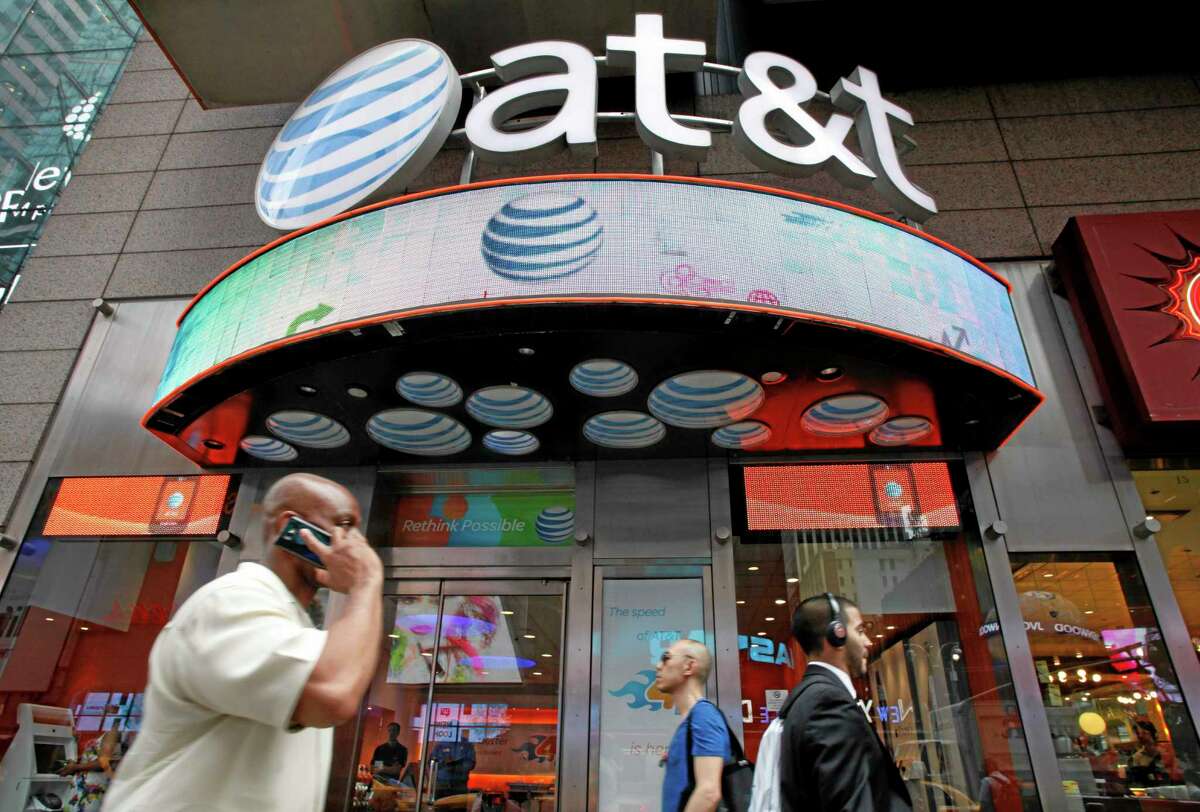 FILE - In this July 11, 2013 photo, a man uses a cell phone as he walks past an AT&T store in New York. (AP Photo/Mark Lennihan, File)