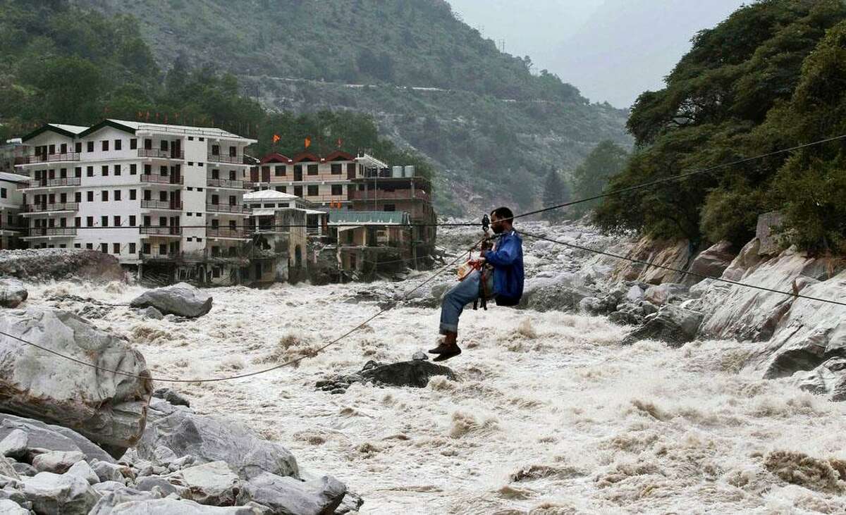 An Indian man crosses over a swollen river with the help of a rope in Govindghat, India, Sunday, June 23, 2013. Bad weather hampered efforts Sunday to evacuate thousands of people stranded in the northern India state of Uttarakhand, where at least 1,000 people have died in monsoon flooding and landslides, army officials said. (AP Photo/Rafiq Maqbool)