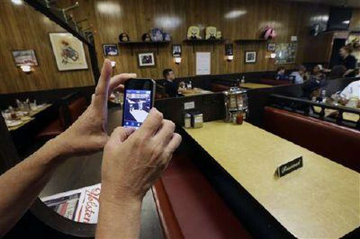 Liz O'Neil, of Montclair, N.J., takes a photograph of a reserved booth where the last show of the HBO series "The Sopranos" was filmed at Holsten's ice cream parlor, Wednesday, June 19, 2013, in Bloomfield, N.J. The sign was put on the booth where the last scene was filmed in honor of actor James Gandolfini who died Wednesday in Italy. He was 51. (AP Photo/Julio Cortez)