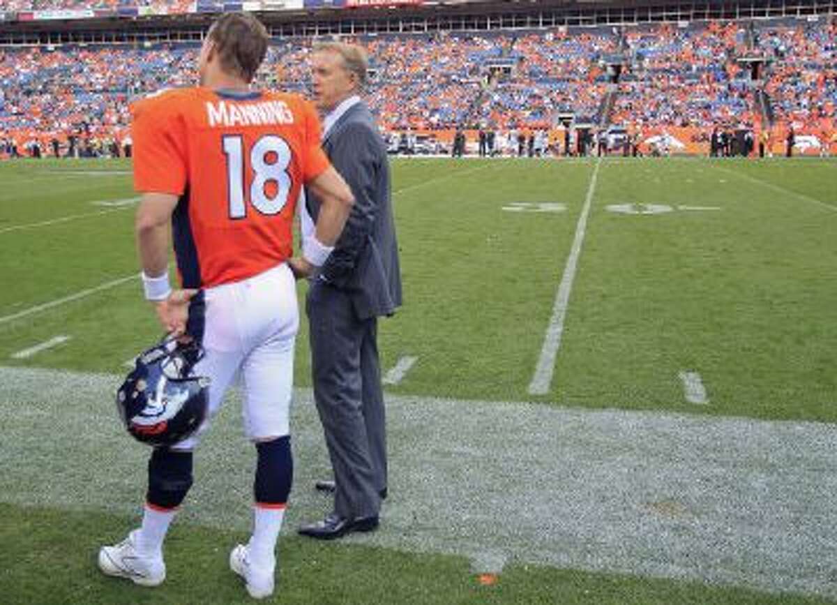 Denver Broncos quarterback Peyton Manning stands on the sidelines next to John Elway.
