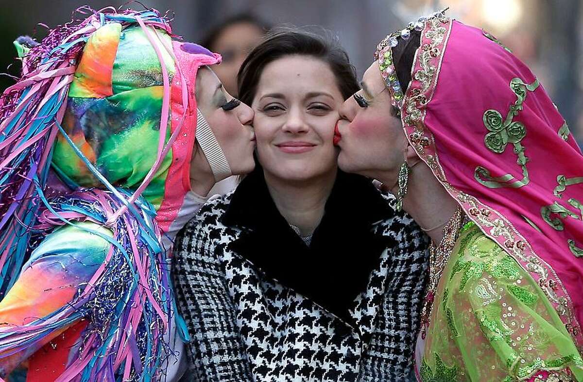 Actress Marion Cotillard, of France, center, the Hasty Pudding Woman of the Year, is kissed by Harvard University theatrical students Renee Rober, left, and Ben Moss, right, as they ride in the back of a convertible during a parade through Harvard Square, in Cambridge, Mass., Thursday, Jan. 31, 2013. The award was presented to Cotillard by Hasty Pudding Theatricals, a theatrical student society at Harvard University. (AP Photo/Steven Senne)