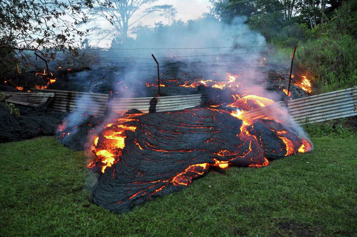 This Tuesday, Oct. 28, 2014 photo provided by the U.S. Geological Survey shows lava that has pushed through a fence marking a property boundary above the town of Pahoa on the Big Island of Hawaii. After weeks of slow, stop-and-go movement, a river of asphalt-black lava was less than the length of a football field from homes in the Big Island community Tuesday. The lava flow easily burned down an empty shed at about 7:30 a.m., several hours after entering a residential property in Pahoa Village, said Hawaii County Civil Defense Director Darryl Oliveira. A branch of the molten stream was less than 100 yards (90 meters) from a two-story house. It could hit the home later Tuesday if it continues on its current path, Oliveira estimated. Residents of Pahoa Village, the commercial center of the island's rural Puna district south of Hilo, have had weeks to prepare for what's been described as a slow-motion disaster. Most have either already left or are prepared to go. (AP Photo/U.S. Geological Survey)