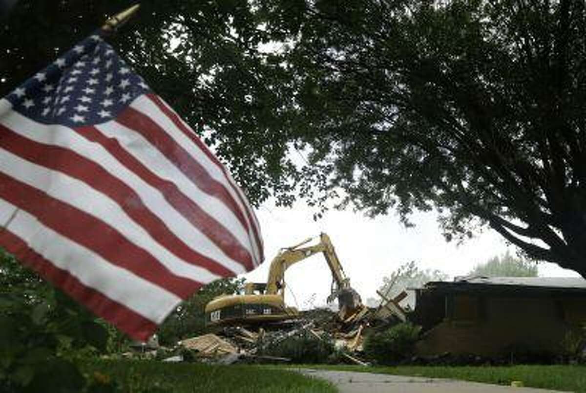 An American flag planted by the curb in front of this home waves in the breeze as tractor operator Jeff Holveck, a volunteer from Cleburne, Texas, demolishes the home Friday, May 31, 2013, in West, Texas. The white slabs popping up across town are a sign that the effort to rebuild West has just begun, almost two months after an explosion that killed 15, and injured 200. (AP Photo/Tony Gutierrez)