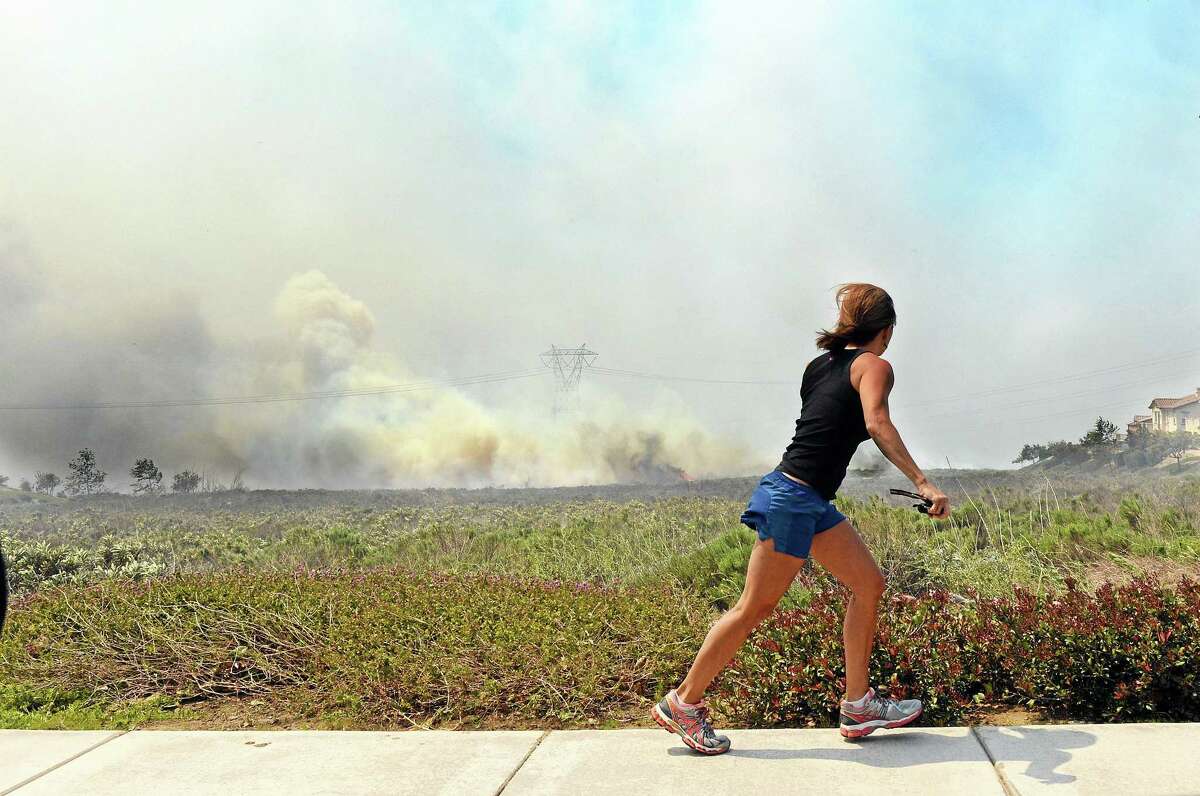 A resident talks on her phone as she watches the Etiwanda Fire in Rancho Cucamonga, Calif., Wednesday, April 30, 2014. The wildfire driven by surging Santa Ana winds sent a choking pall of smoke through foothill neighborhoods, forcing the evacuation of at least 1,650 homes and the closure of at least seven schools. No homes burned, but the smoke prompted mandatory evacuation orders for several areas of town nestled at the base of the San Bernardino Mountains east of Los Angeles. More than 500 firefighters battled the flames near this city of 165,000 people. The fire was reported about 8 a.m., grew to 200 acres by noon, quadrupled in size within a few hours and continued to grow as it roared through dry brush.(AP Photo/Inland Valley Daily Bulletin, Will Lester)