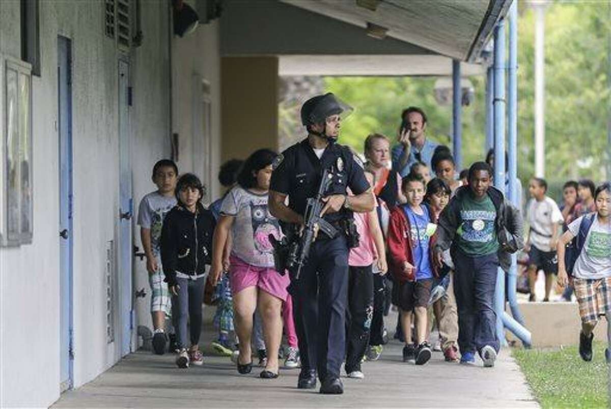A Santa Monica police officer leads children on a field trip from Citizens of the World Charter School in Los Angeles out of Santa Monica College, where they had gone for a planetarium show, following a shooting in the area, in Santa Monica, Calif., Friday, June 7, 2013. Two people were found dead Friday in a burned home near the campus, where someone sprayed a street corner with gunfire. (AP Photo/Reed Saxon)