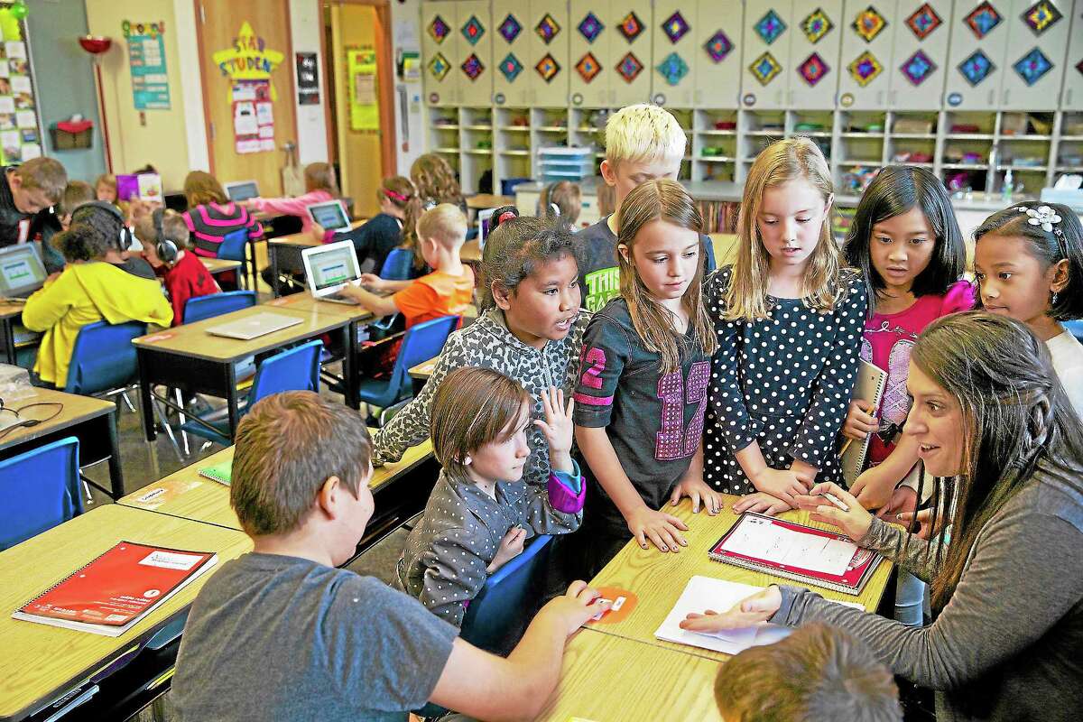 In this Oct. 9, 2013 photo, third grade teacher Janell Cooke talks with a group of students about a story they are working on as other students work on concentrated vocabulary at Tualatin Elementary in Tualatin, Ore.
