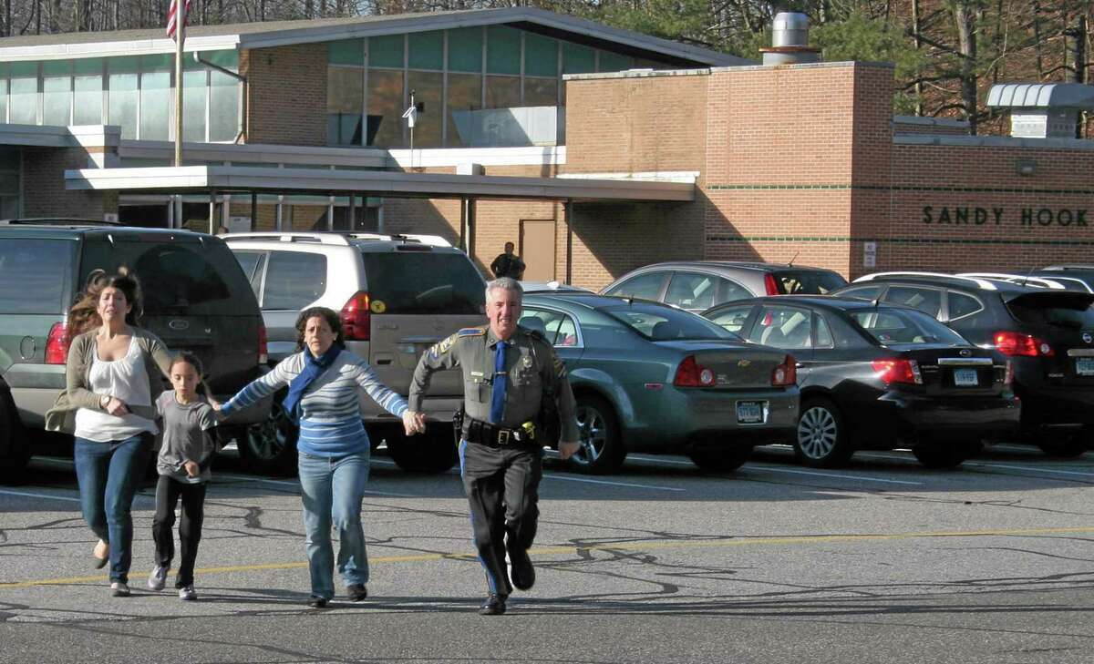 FILE - In this Friday, Dec. 14, 2012, file photo provided by the Newtown Bee, a police officer leads two women and a child from Sandy Hook Elementary School in Newtown, Conn., where a gunman opened fire, killing 26 people, including 20 children. AP Photo/Newtown Bee, Shannon Hicks, File)