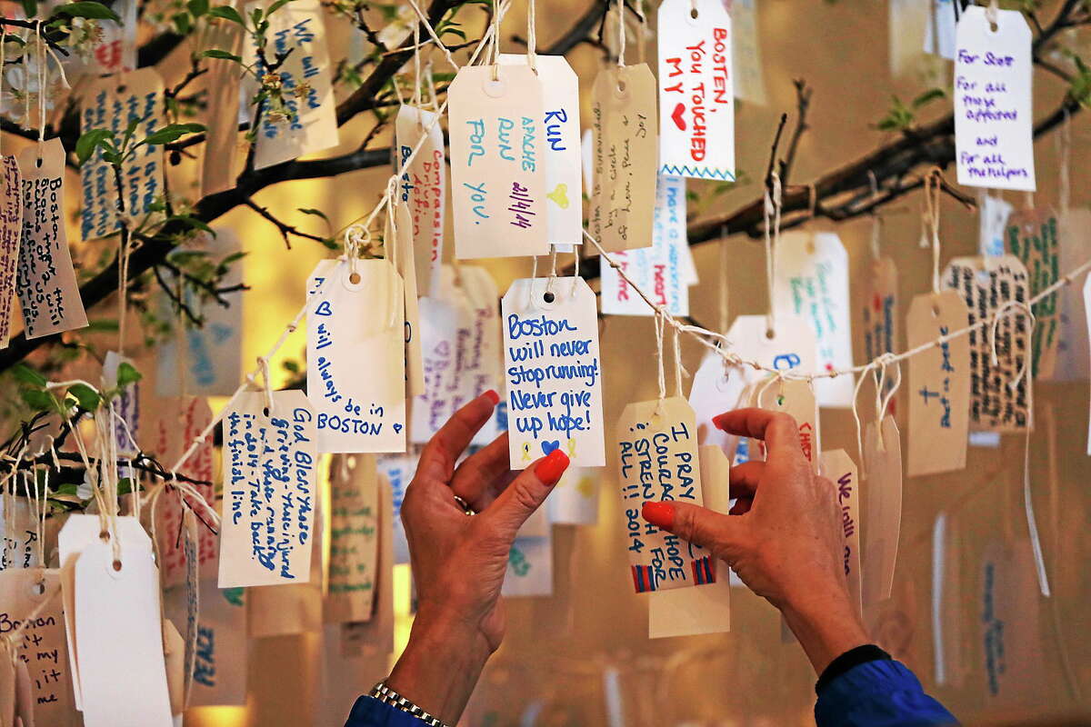 A visitor hangs a message on a tree at the “Dear Boston” exhibit at the Boston Public Library on April 20, 2014 in Boston. The exhibit features a collection of items from the marathon bombing memorial.