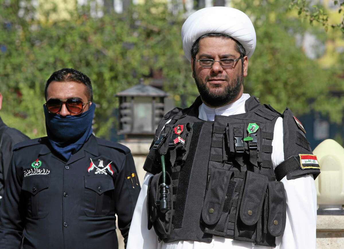 An Iraqi Shiite cleric, right, wears a military vest as he watches a parade of Shiite militiamen, in the mostly Kurdish northern oil rich province of Kirkuk, Iraq, Saturday June 21, 2014. Thousands of heavily-armed Shiite militiamen paraded through several Iraqi cities on Saturday as Sunni militants seized two strategically located towns in what appeared to be a new offensive in the western Anbar province. (AP Photo/Hussein Malla)