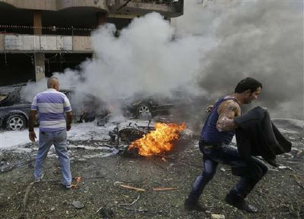 A Lebanese man runs past a burned car at the scene where two explosions have struck near the Iranian Embassy, killing many, in Beirut, Lebanon.
