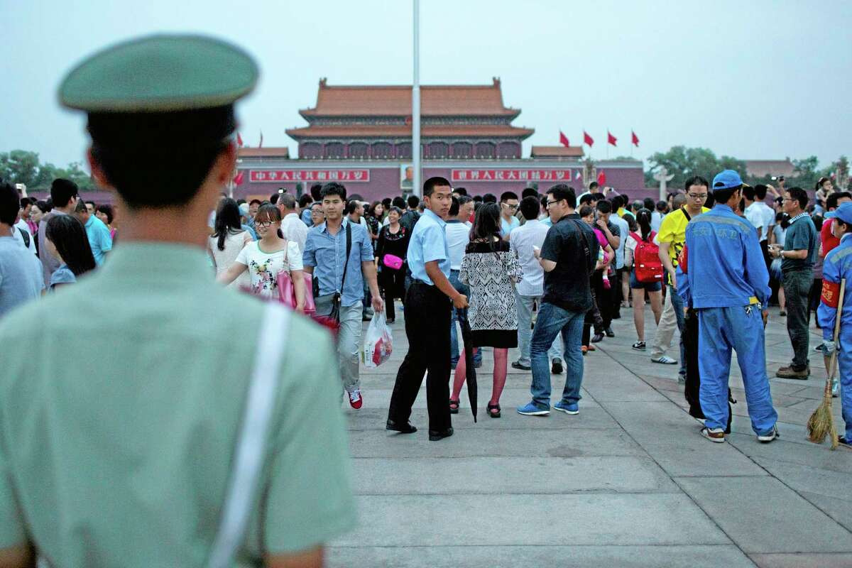 A paramilitary policeman in plain clothes with an umbrella, center, looks back as his uniformed comrade, foreground left, holds his position during a flag-lowering ceremony on Tiananmen Square in Beijing, China, Wednesday, June 4, 2014. Heavy security blanketed central Beijing on the 25th anniversary of the bloody suppression of the Tiananmen Square pro-democracy protests on Wednesday, pre-empting any attempts to publicly commemorate one of the darkest chapters in recent Chinese history. (AP Photo/Alexander F. Yuan)