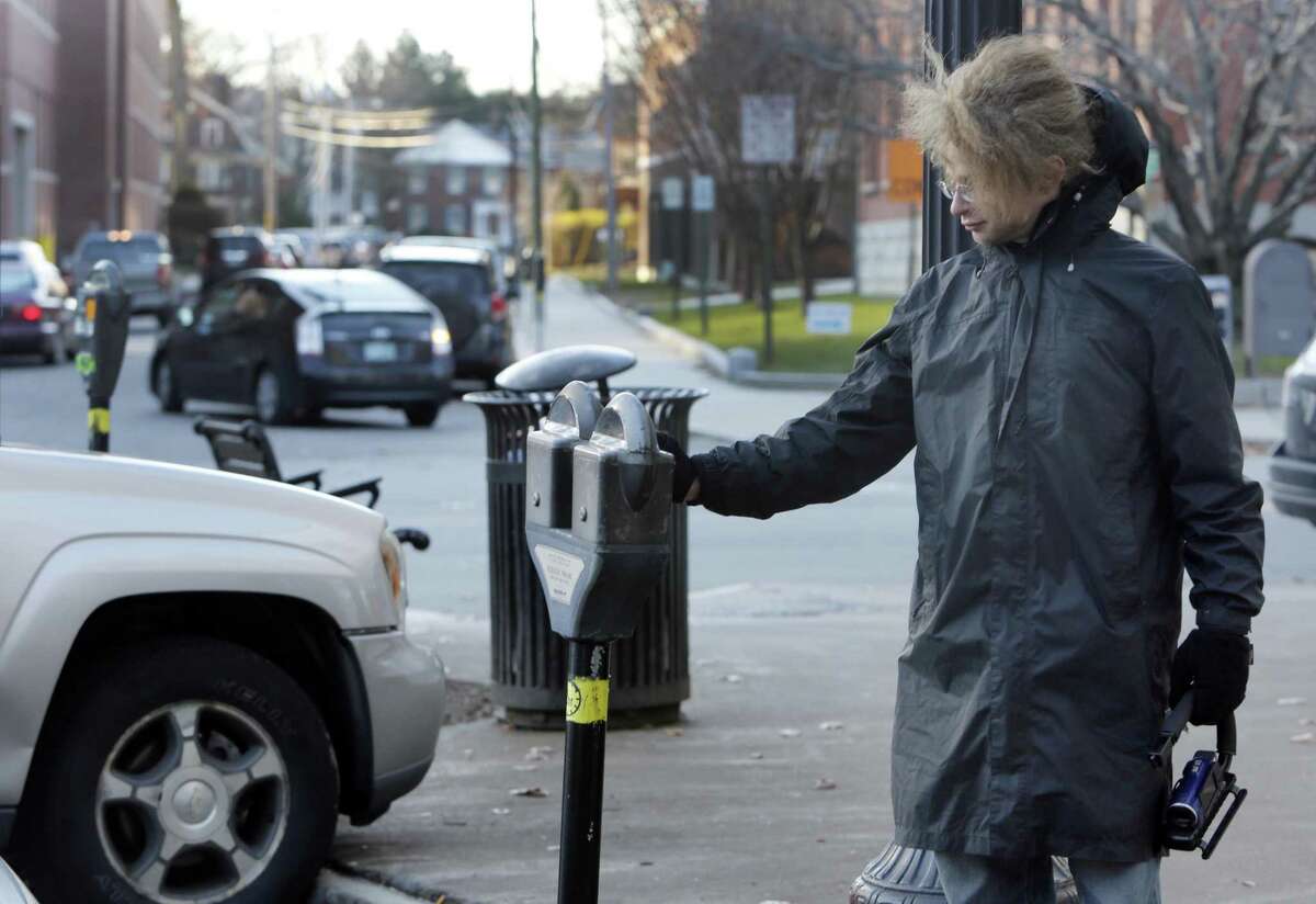 In this photo taken Wednesday Nov. 19, 2014 one of many self-proclaimed ìRobin Hoodersî Garret Ean puts money in expired meters ahead of parking enforcement officers on Main St. in Keene, N.H. A merry band of Keene activists stalk parking enforcement officers, pumping quarters into expired meters before the officers write tickets. But city officials say their practice of taunting and videotaping the officers interferes with their work and stresses them out. The New Hampshire Supreme Court is deliberating if there is a line to be drawn between constitutionally-protected free speech rights and protecting government employees from harassment. (AP Photo/Jim Cole)
