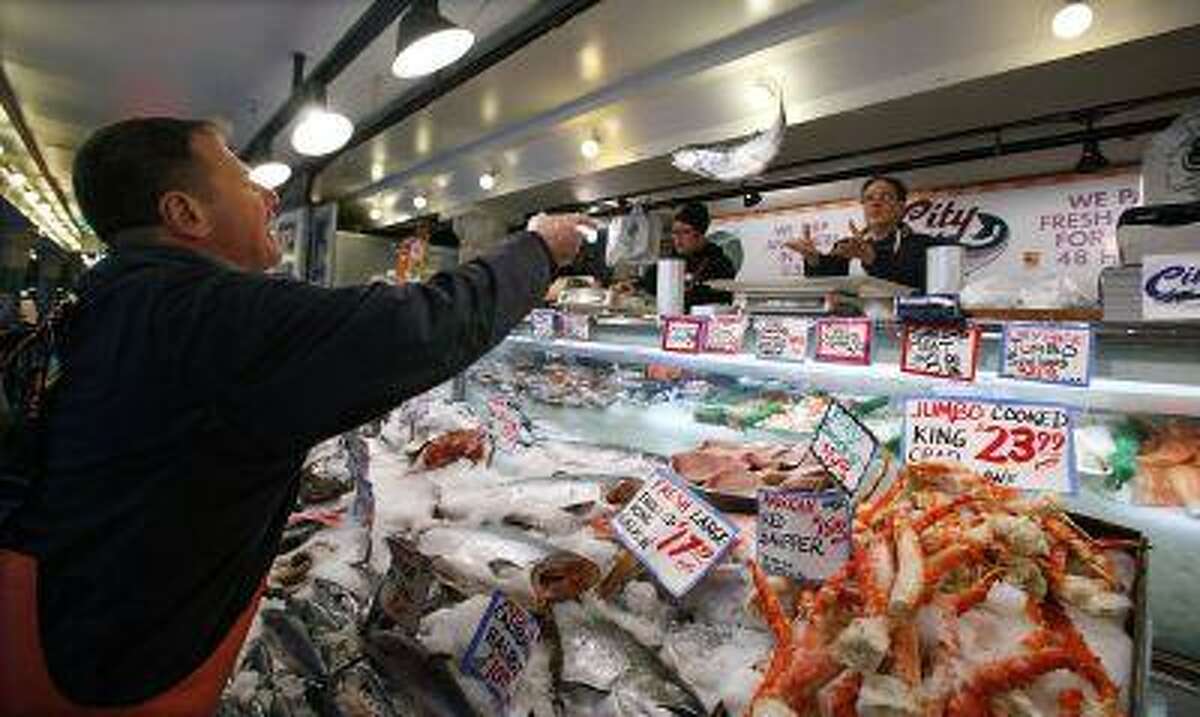 Fish vendor Eddy Adams, left, tosses a salmon to Robert Shapiro to be prepped for a customer at the City Fish Co. in the historic Pike Place Market, Thursday, Feb. 3, 2011, in Seattle. The 103-year old market is part-way through a several-year renovation project that's replacing core infrastructure systems and upgrading seismic stability. Most of the businesses continue to operate, with some temporarily moved to nearby locations. (AP Photo/Elaine Thompson)