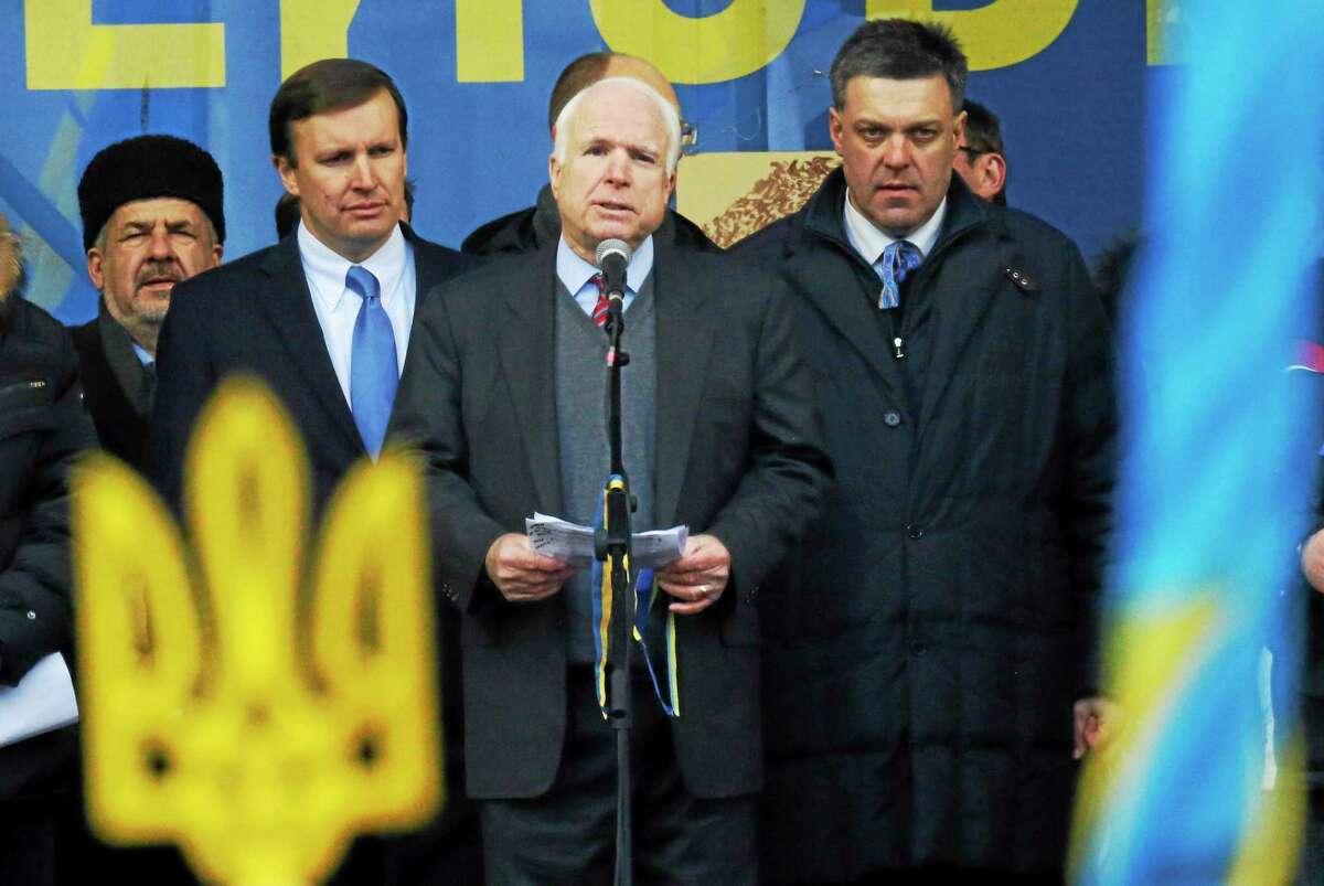 U.S. Senator John McCain, center, speaks as Democratic senator from the state of Connecticut, Chris Murphy, second left, and Opposition leader Oleh Tyahnybok, right, stand around him during a Pro-European Union rally in Independence Square in Kiev, Ukraine, Sunday, Dec. 15, 2013. Ukrainian national symbol is in the foreground.