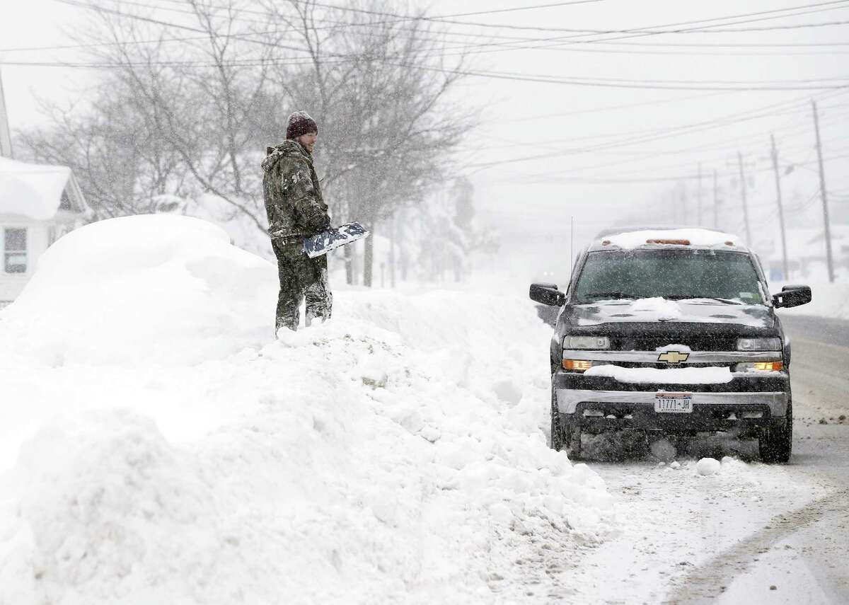 Jeremy Bauer stands on a snowbank next to a buried car outside his brother’s house on Wednesday, Nov. 19, 2014, in Lancaster, N.Y. Lake-effect snow pummeled areas around Buffalo for a second straight day, leaving residents stuck in their homes as officials tried to clear massive snow mounds with another storm looming.