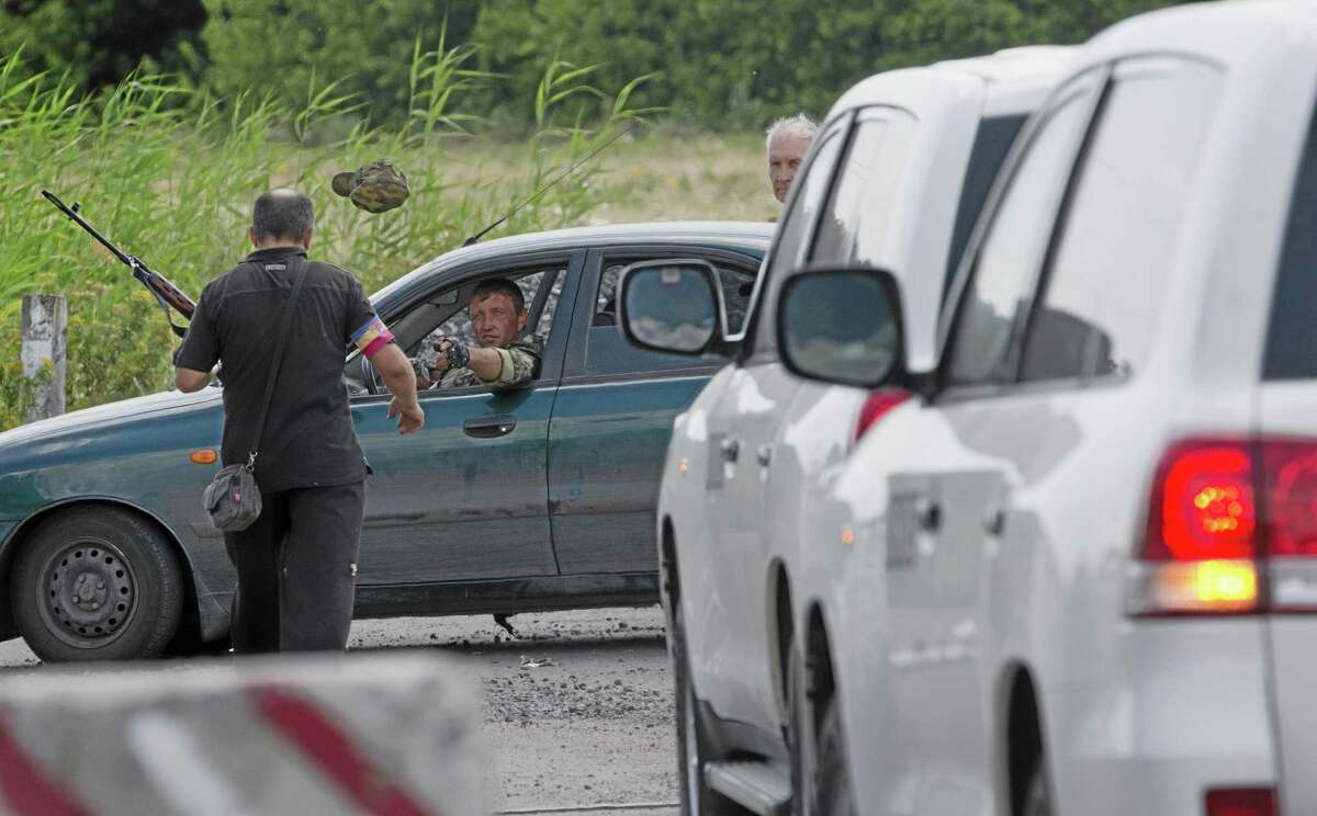 A pro-Russian rebel throws a hat to his comrade to keep uniform formality as the convoy of the OSCE mission in Ukraine approaches to a check-point near the village of Rassipne, near the scene of the Malaysia Airlines plane crash, Donetsk region, eastern Ukraine, Thursday, July 31, 2014. (AP Photo/Dmitry Lovetsky)