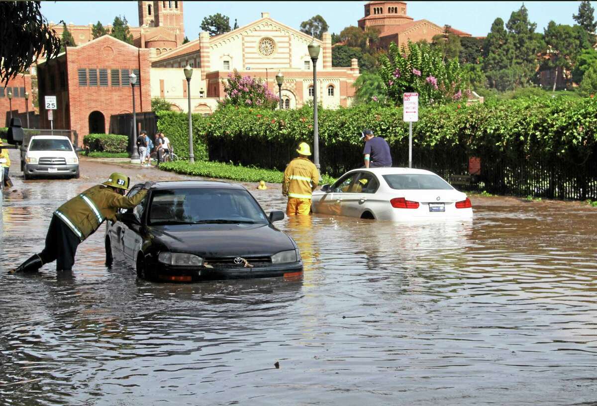 Los Angeles firefighters help drivers whose cars became stranded on Sunset Boulevard after a 30-inch water main broke and sent water flooding down Sunset and onto the UCLA campus, background, in the Westwood section of Los Angeles on Tuesday, July 29, 2014.(AP Photo/Steve Gentry)