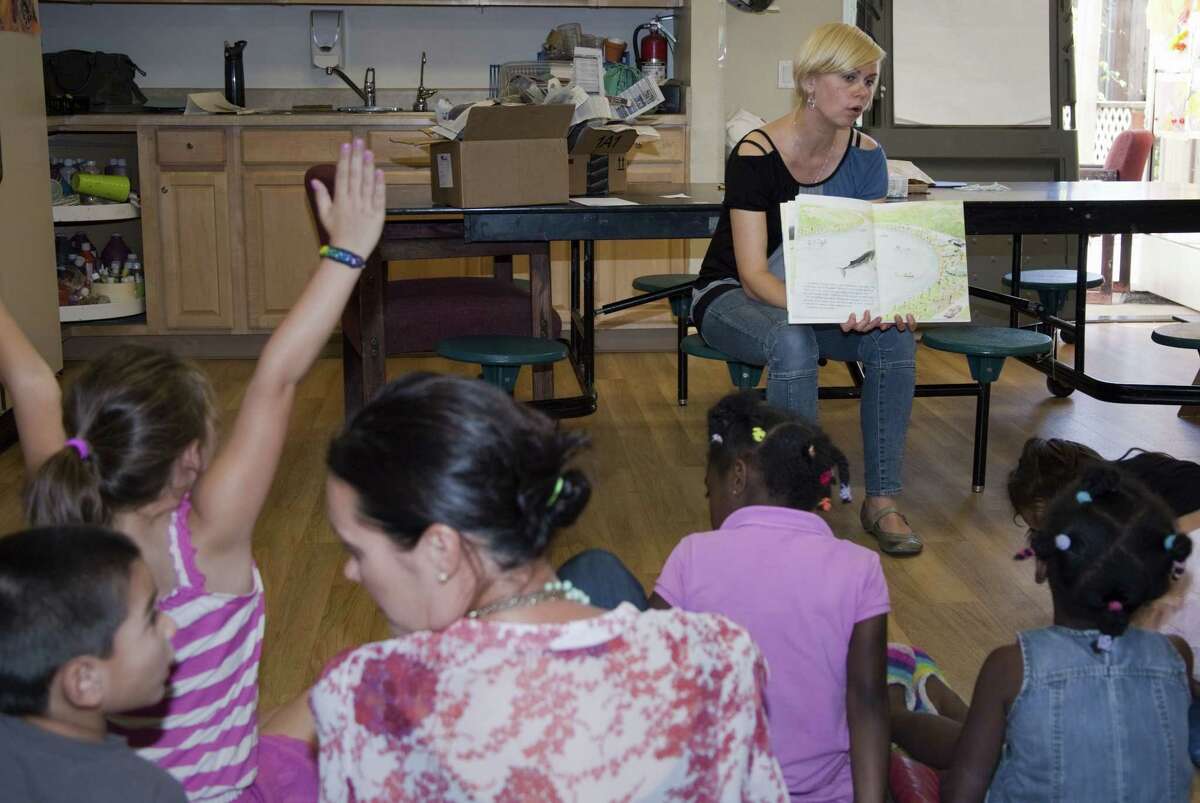 In this June 2014 photo provided by Transition House, a homeless shelter in Santa Barbara, Calif., Nicole Janowicz, a member of Transition House childrenís program staff, reads a story to children before dinner as part of Transition Houseís Technology and Literacy for Children program.