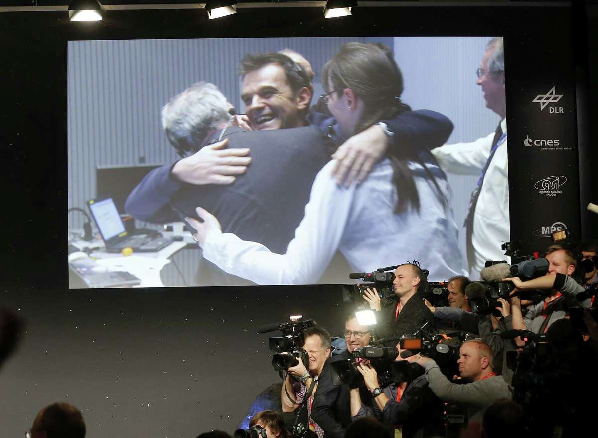FILE -In this Nov. 12, 2014 file picture celebrating scientists in the control room appear on a video screen at the European Space Agency ESA after the Rosetta's Philae landed on comet 67P/Churyumov-Gerasimenko, in Darmstadt, Germany. Philae landed next to a cliff that largely blocked sunlight from reaching its solar panels on the comet. The head of the European comet mission says scientists will listen for signals from the Philae lander Saturday Nov. 15, 2014 but think it is unlikely they will establish any kind of communication soon. Controllers at the European Space Agency on Friday ordered the lander to perform a maneuver intended to pull it out of a shadow on the comet so that solar panels could recharge the depleted batteries. ìWe donít know if the charge will ever be high enough to operate the lander again,î Paolo Ferri, ESAís head of mission operations, told The Associated Press. (AP Photo/Michael Probst)