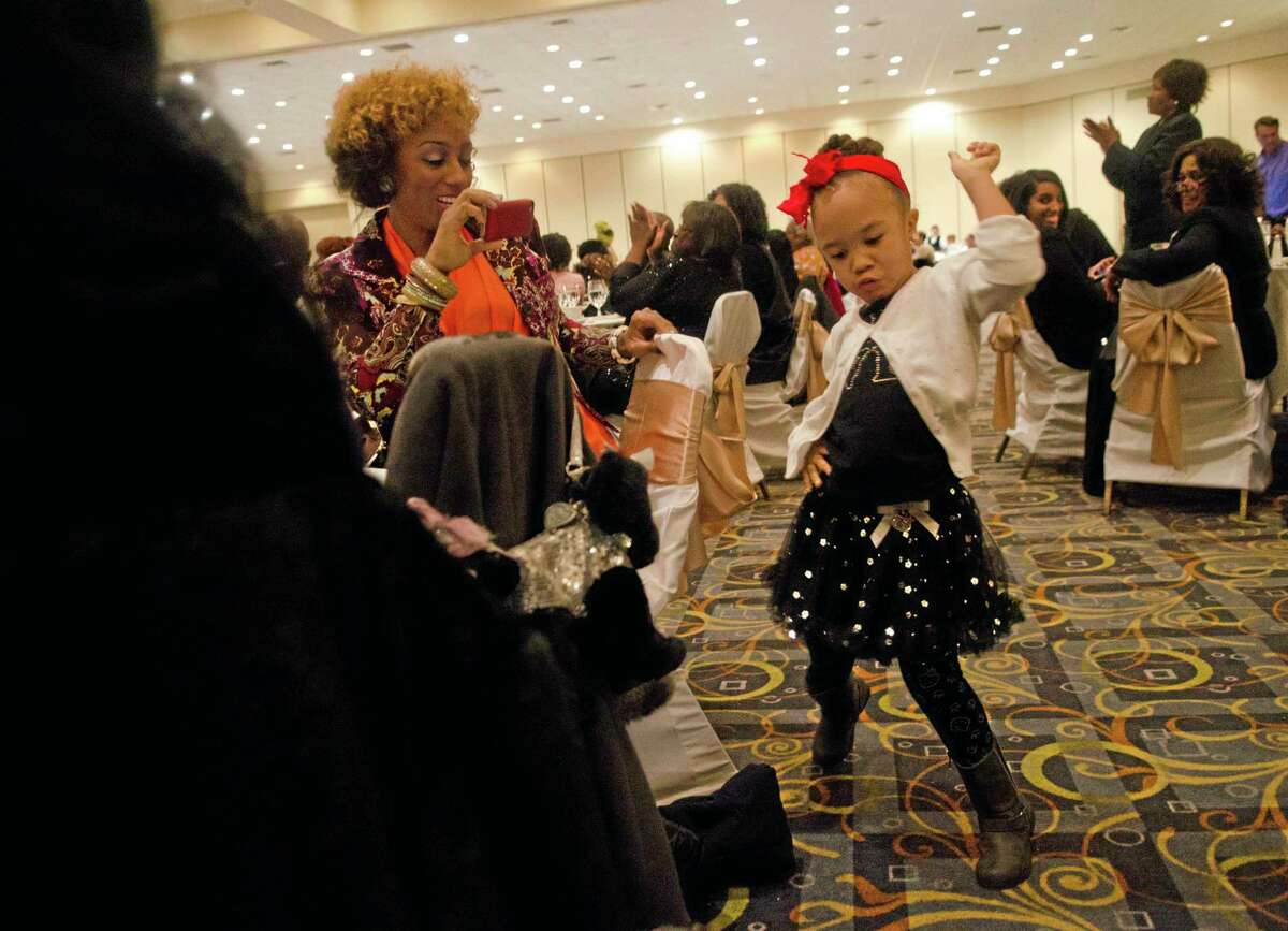 Flint artist Brinae Ali records her daughter Malaika Bradley, 4, dancing to Grammy winning singer Regina Belle perform during the 13th Annual Black History Month Brunch, hosted by the Genesee District Library at the Riverfront Banquet Center on Saturday, Feb. 8, 2014. (AP Photo/MLive.com, Samuel Wilson)