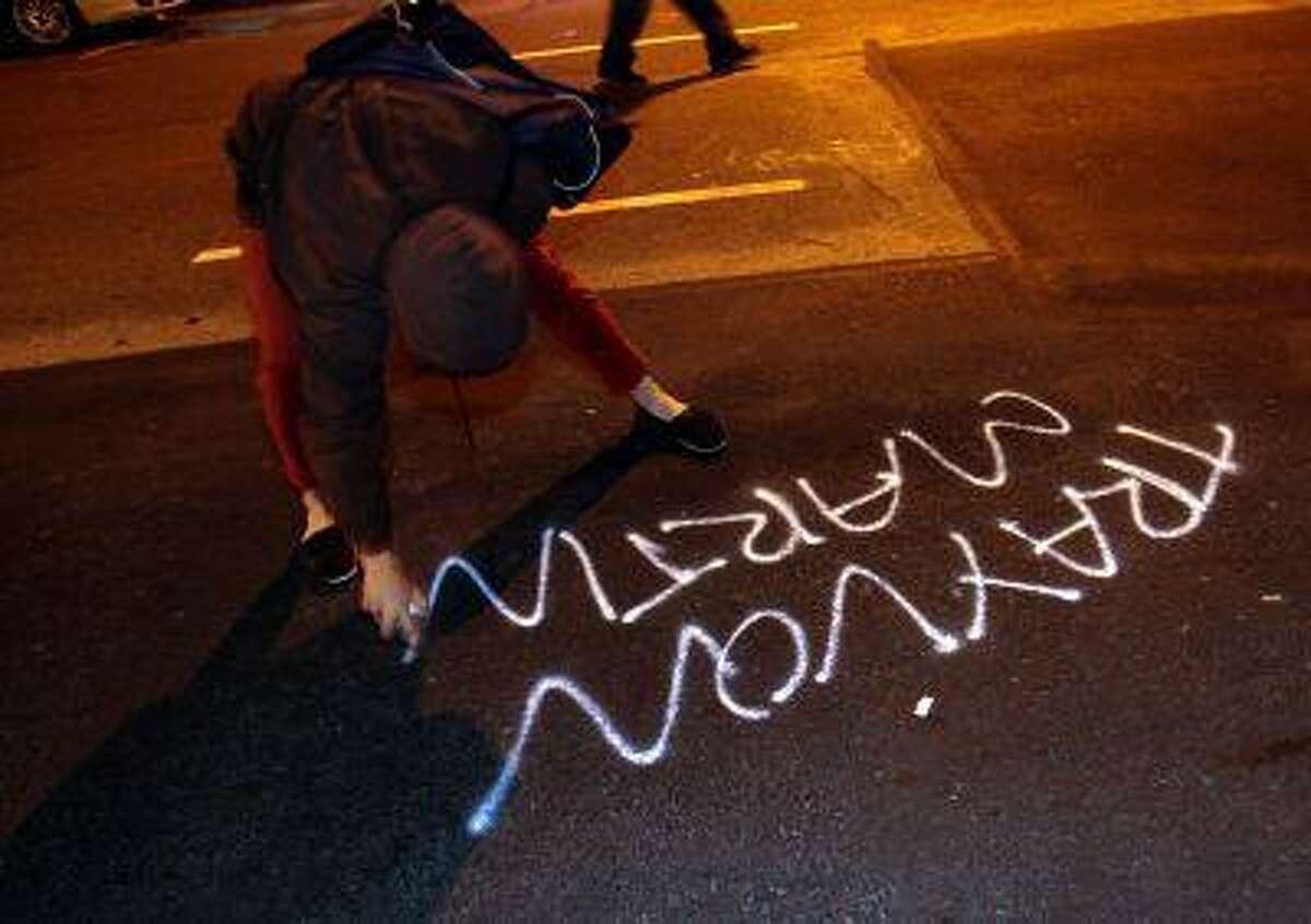 A woman spray paints along Franklin Street during a protest after George Zimmerman was found not guilty in the 2012 shooting death of teenager Trayvon Martin, early Sunday, July 14, 2013, in Oakland, Calif.